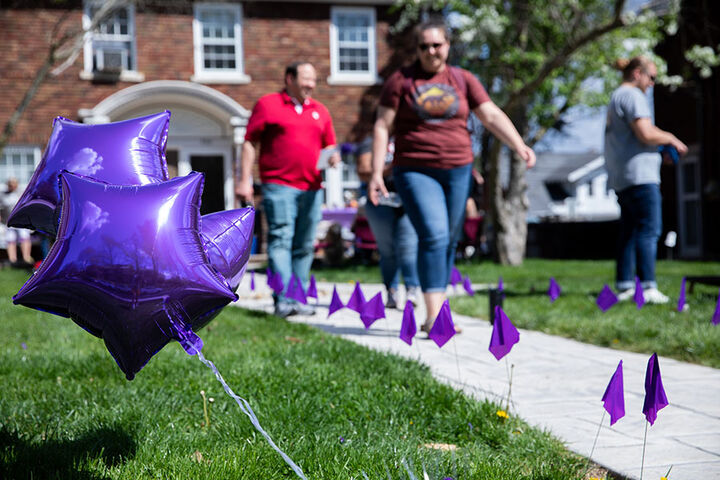 People walk along a sidewalk decorated with purple flags and balloons.